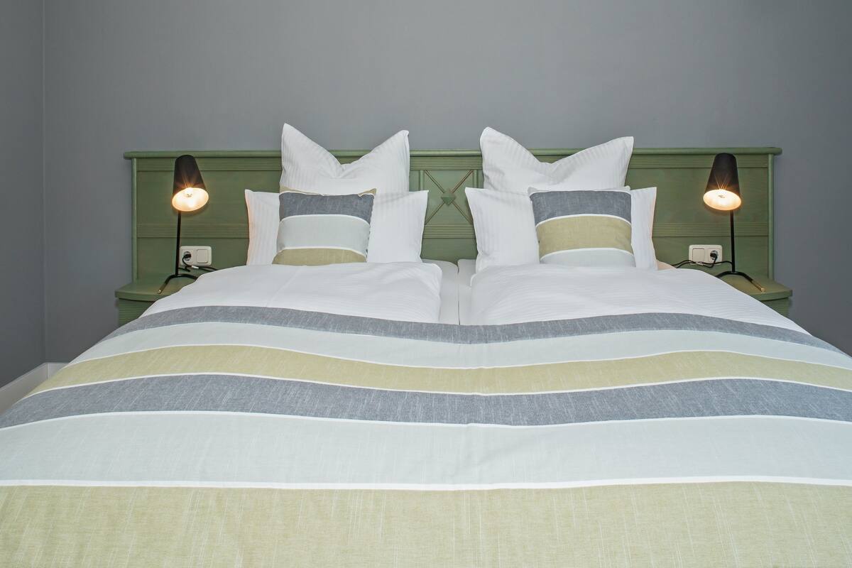 A bed with a striped bedspread, two bedside lamps, and a green headboard.