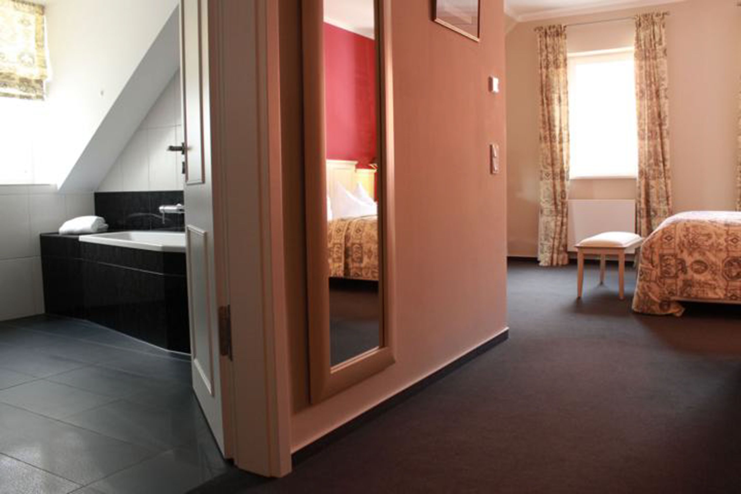 A hotel room with a bathroom, a bed, a chair, and a window with curtains.