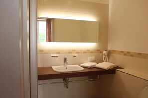 Un baño con lavamanos, espejo, toallero y ducha.