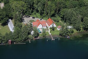 An aerial view of a lakeside property with a main house, dock, and surrounding greenery. - Café Wildau - Hotel am Werbellinsee (Schorfheide)