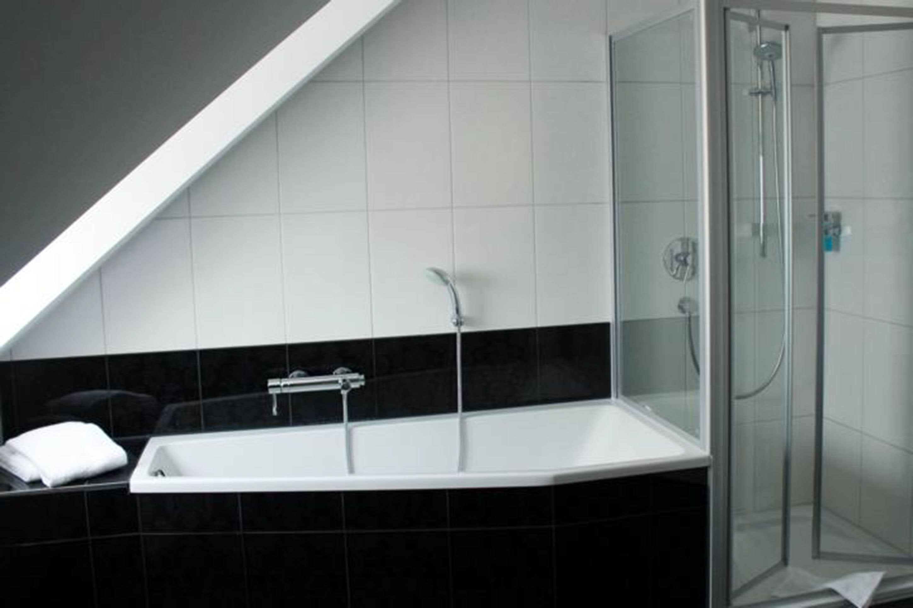 Ein modernes Badezimmer mit freistehender Badewanne, einer Duschkabine und Wänden mit Schwarz-Weiß-Fliesen.