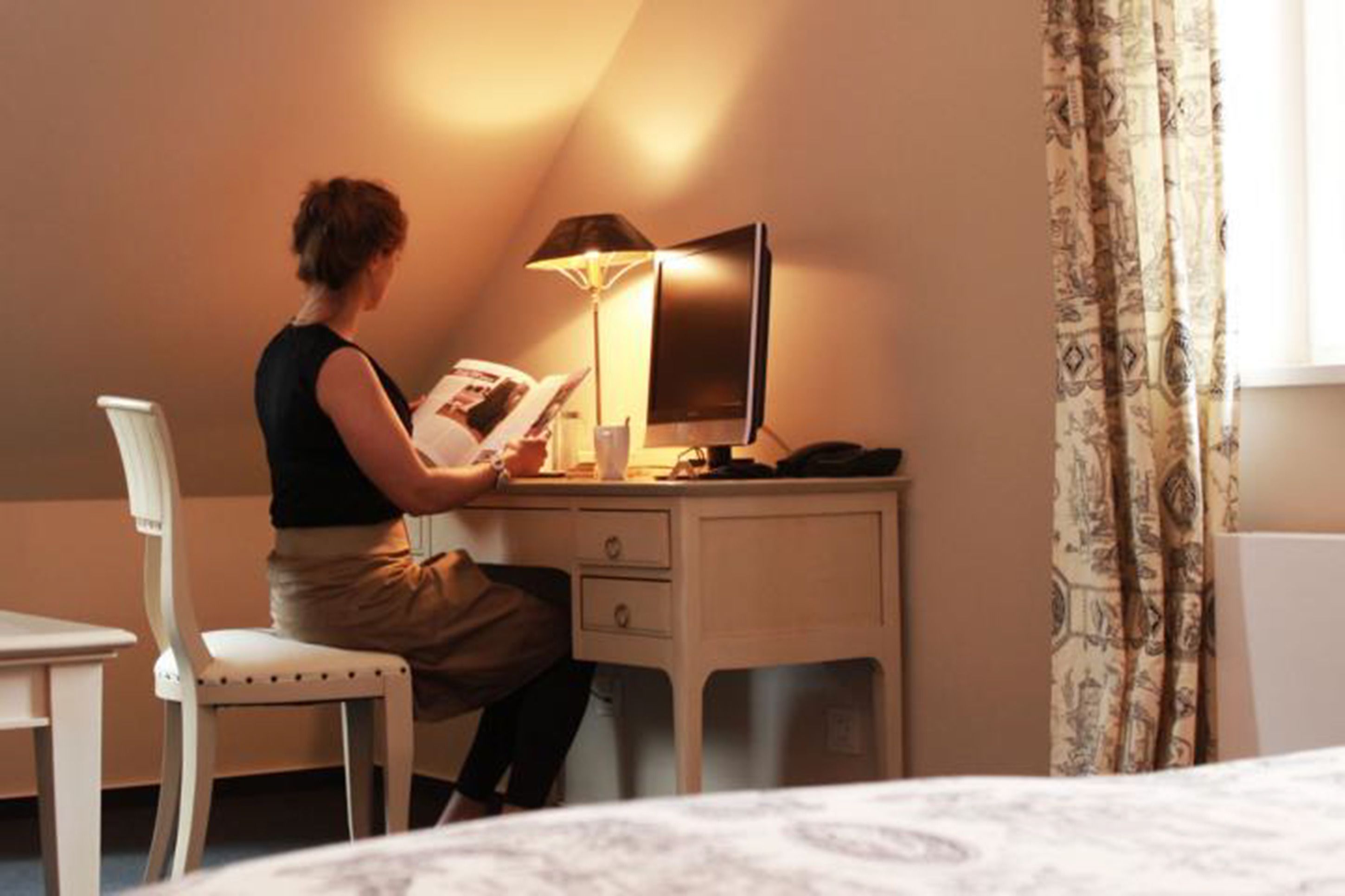 A hotel room with a desk, chair, and a lamp.