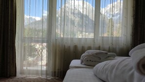A hotel room with a bed, a window with sheer curtains, and a view of mountains. - Iri Busteni Hotel (Busteni)