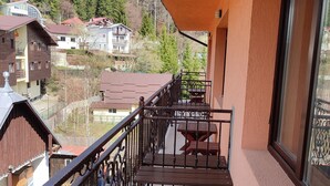 A balcony with a wooden table and chairs, a metal railing, and a view of houses and trees. - Iri Busteni Hotel (Busteni)