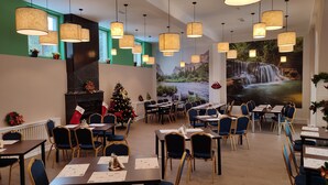 A restaurant with multiple tables and chairs, hanging pendant lights, a Christmas tree, and a fireplace. - Iri Busteni Hotel (Busteni)