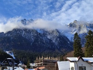 A mountainous landscape with snow-covered peaks, a cross on a peak, and a village with buildings in the foreground. - Iri Busteni Hotel (Busteni)