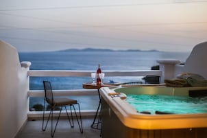 Un balcón con una silla, una mesa con una botella y vasos, y un jacuzzi.