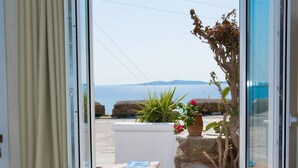 A balcony with a view of the sea, a table with a bottle and glass, and a potted plant. - Villa Elina Suites And More (Mykonos)