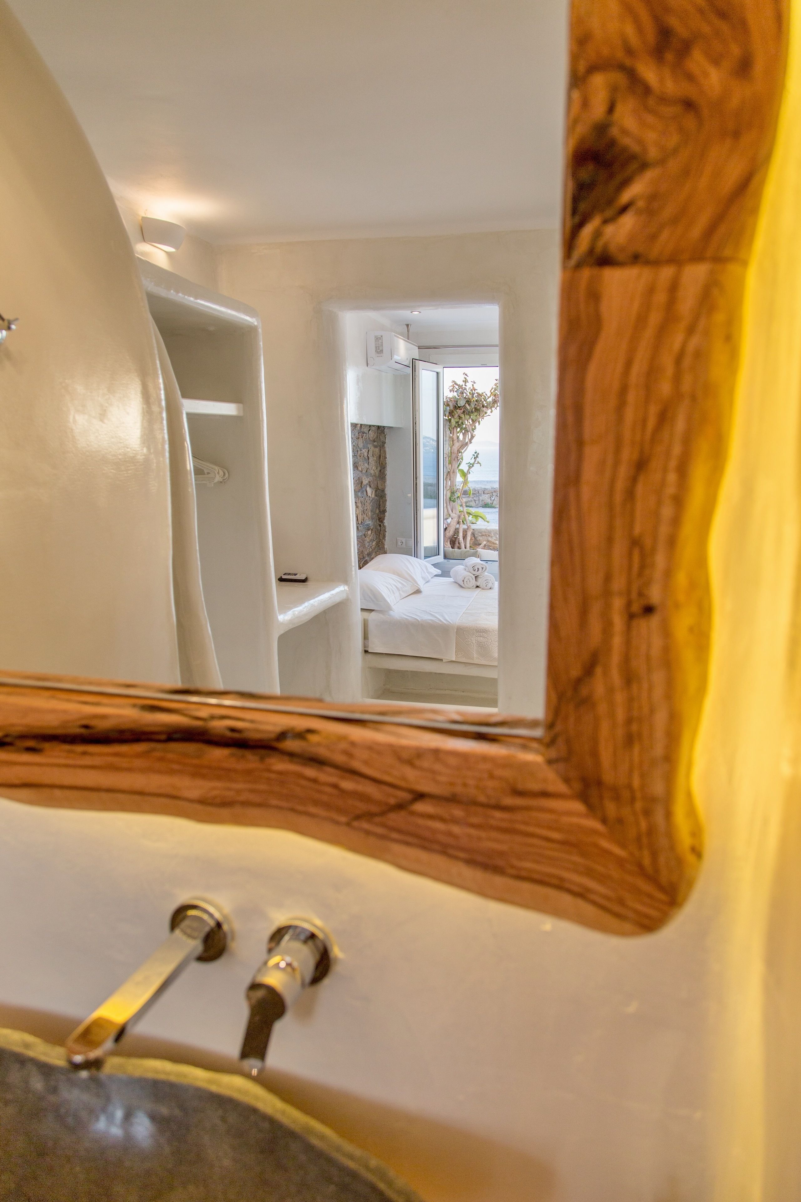 Ein Badezimmer mit Waschbecken, Spiegel und Blick auf ein Schlafzimmer mit Bett und Fenster.