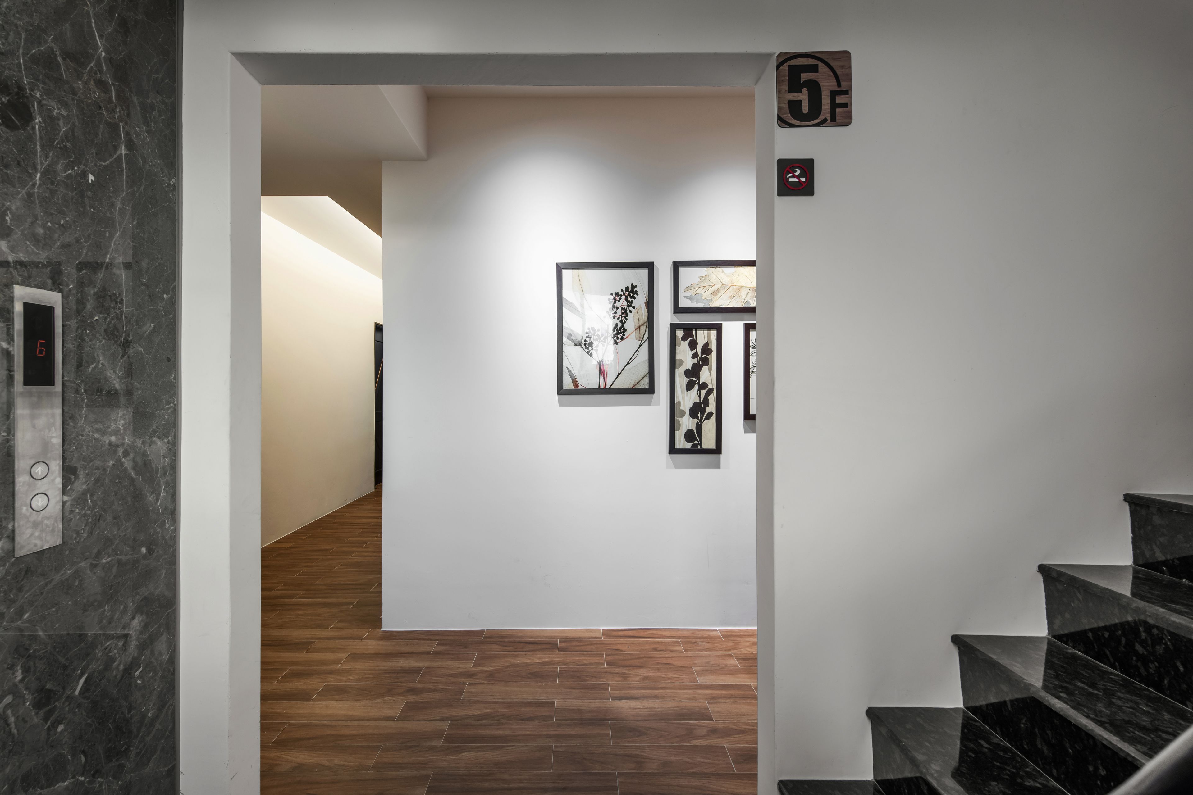 Um interior moderno com escadaria de mármore, piso de madeira e obras de arte emolduradas nas paredes.