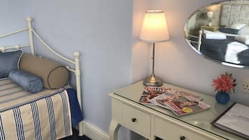 Un lit bien fait, recouvert d’une couverture à rayures, une lampe de chevet, un miroir et un bureau avec un magazine et un petit vase.