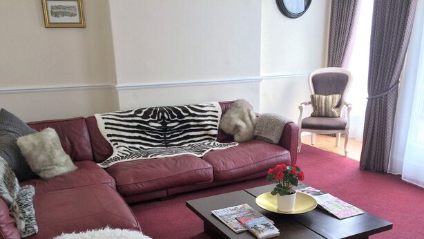 A living room with a red leather sofa, a zebra-patterned throw, a white chair with a striped cushion, and a coffee table with magazines and a vase of red flowers.