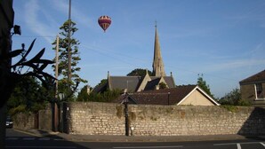 A church with a tall steeple, a stone wall, and a hot air balloon in the sky.