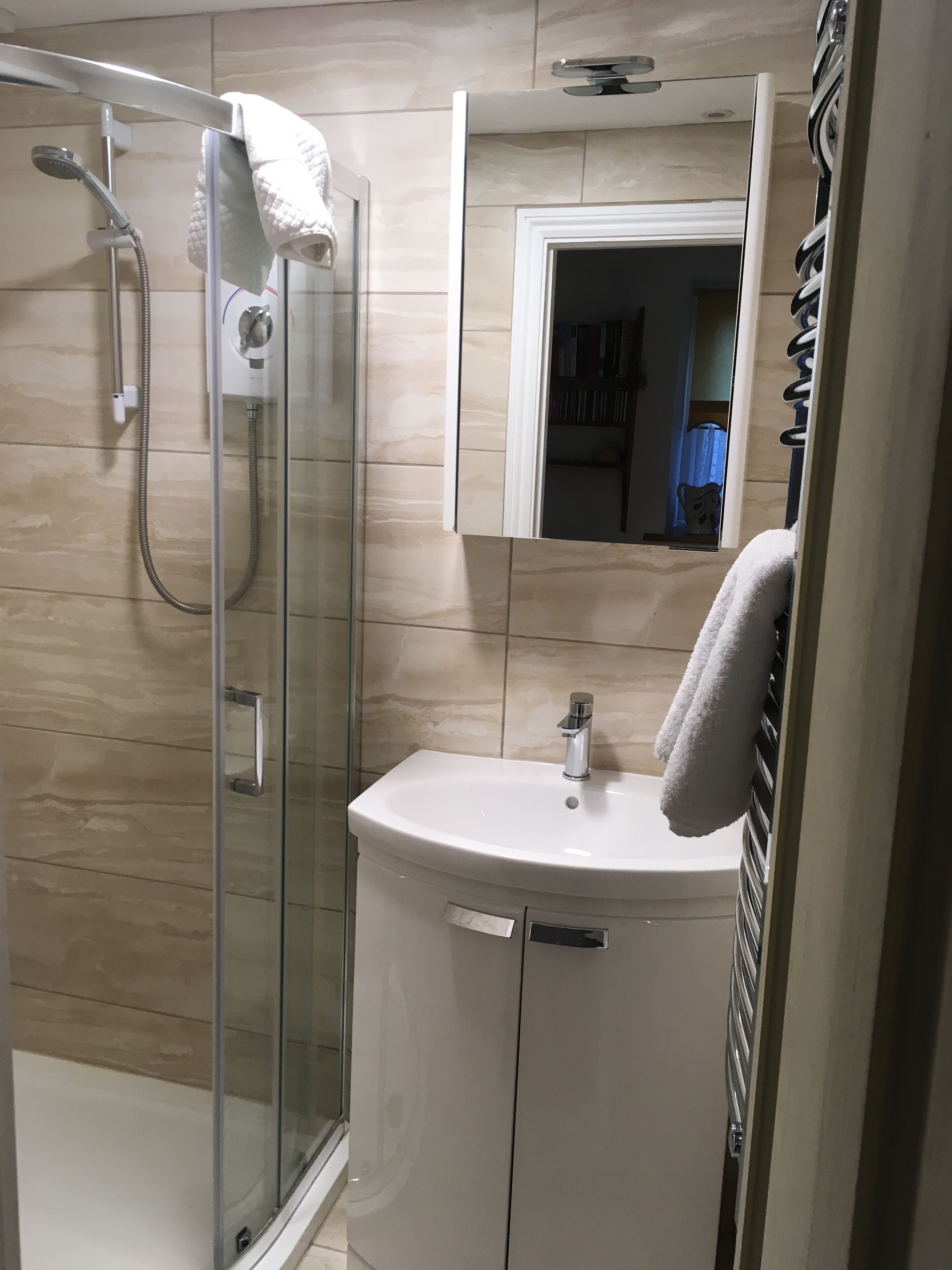 Une salle de bain moderne avec une douche à l’italienne en verre, un lavabo blanc et un miroir au-dessus.