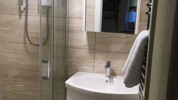 Une salle de bain moderne avec une douche à l’italienne en verre, un lavabo blanc et un miroir au-dessus.
