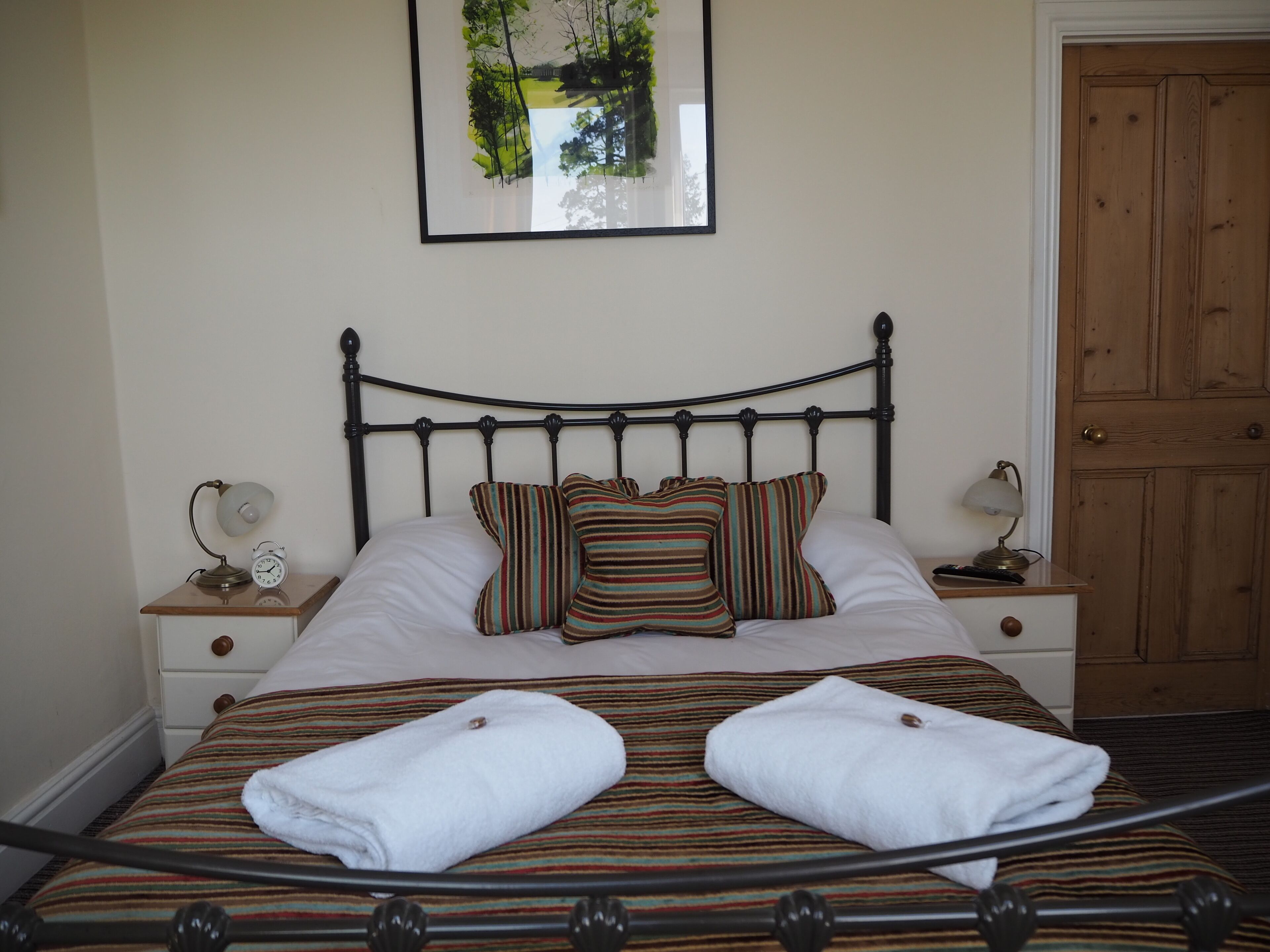 A neatly made bed with striped bedding and two white towels, a bedside table with a lamp, and a framed picture on the wall.