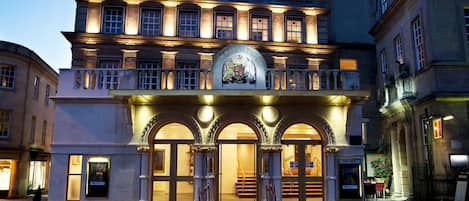 A historic building with a grand entrance, featuring a red carpet and a coat of arms above the doors.