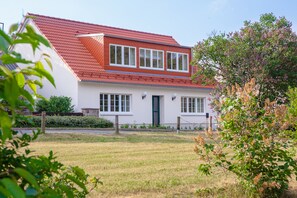 Une maison blanche avec un toit rouge, un porche à l’avant et un petit jardin.