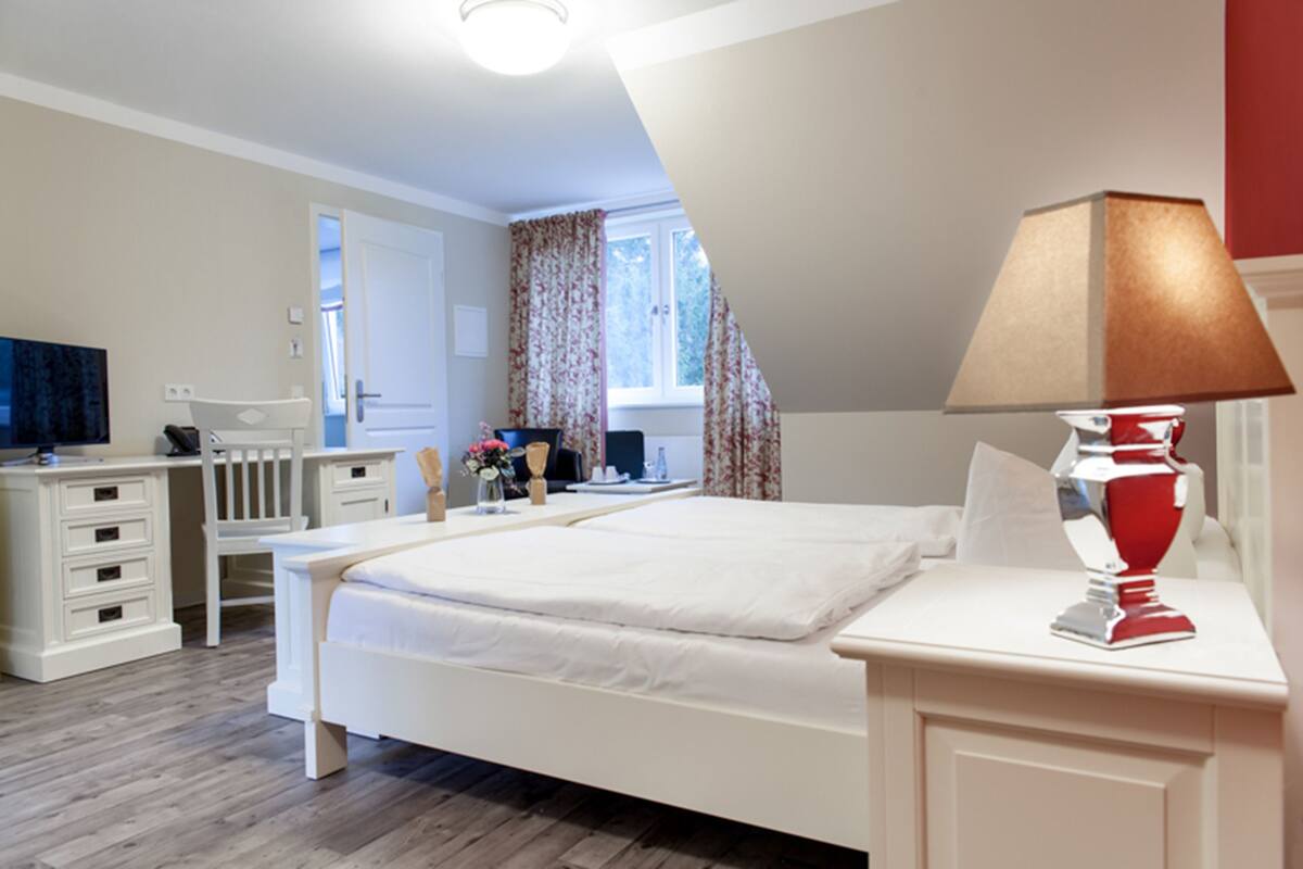 A bedroom with a bed, bedside table, lamp, and a desk with a chair.
