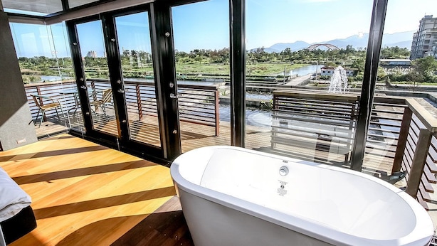 A modern bathroom with a freestanding bathtub, large windows, and a view of a landscaped area with a fountain. - Hiten B&B (Wujie)
