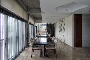 A modern conference room with a long table and patterned chairs, large windows with curtains, and a decorative wall panel.