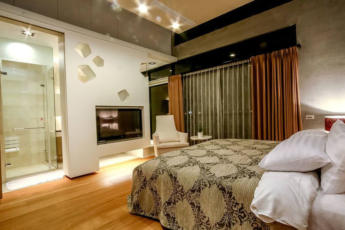 Une chambre moderne dotée d’un grand lit, d’une télévision, d’une douche en verre et d’un coin salon.