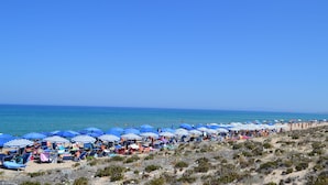 Une plage bordée de rangées de parasols et de chaises de plage aux rayures bleues et blanches.