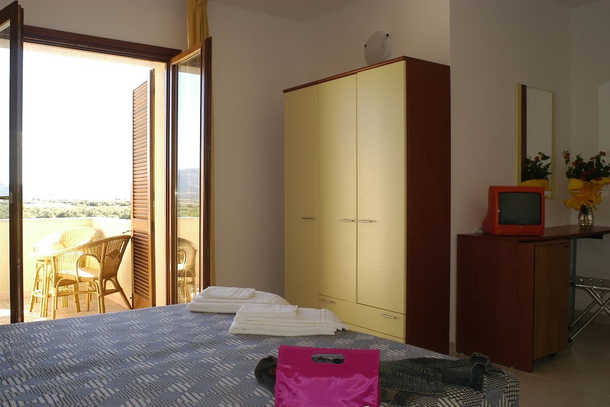 Ein Schlafzimmer mit Bett, Kleiderschrank, Schreibtisch mit Fernseher und Balkon mit Stühlen und Tisch.