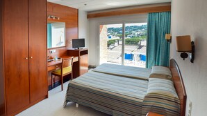 Habitación de hotel con dos camas, un escritorio con computadora, una silla y vistas a la ciudad desde la ventana.