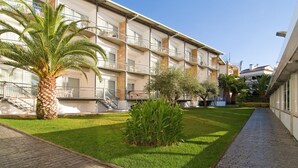 Un hotel de varios pisos con balcones, una palmera y un césped bien cuidado.