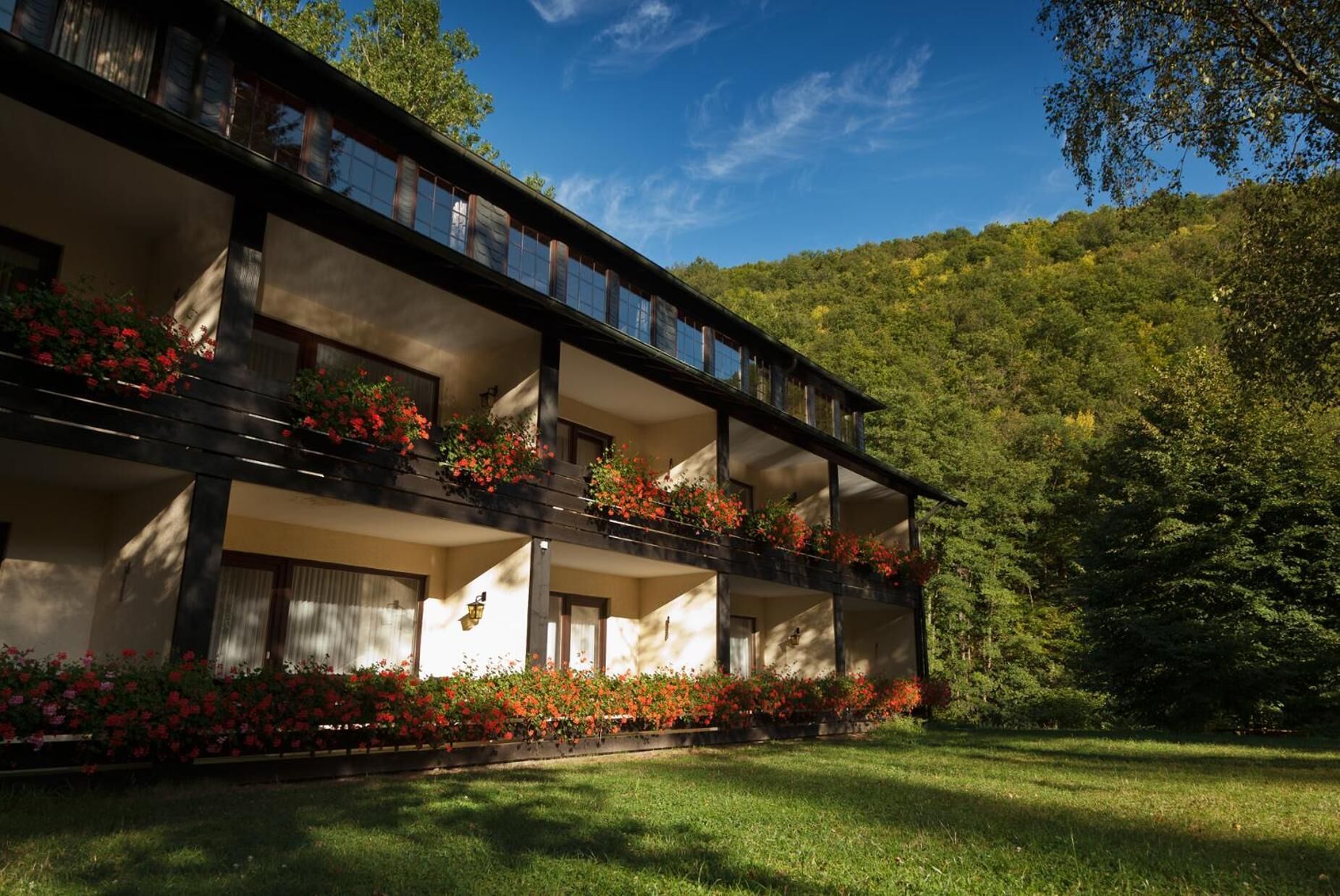A two-story building with balconies, surrounded by lush greenery and a clear sky.