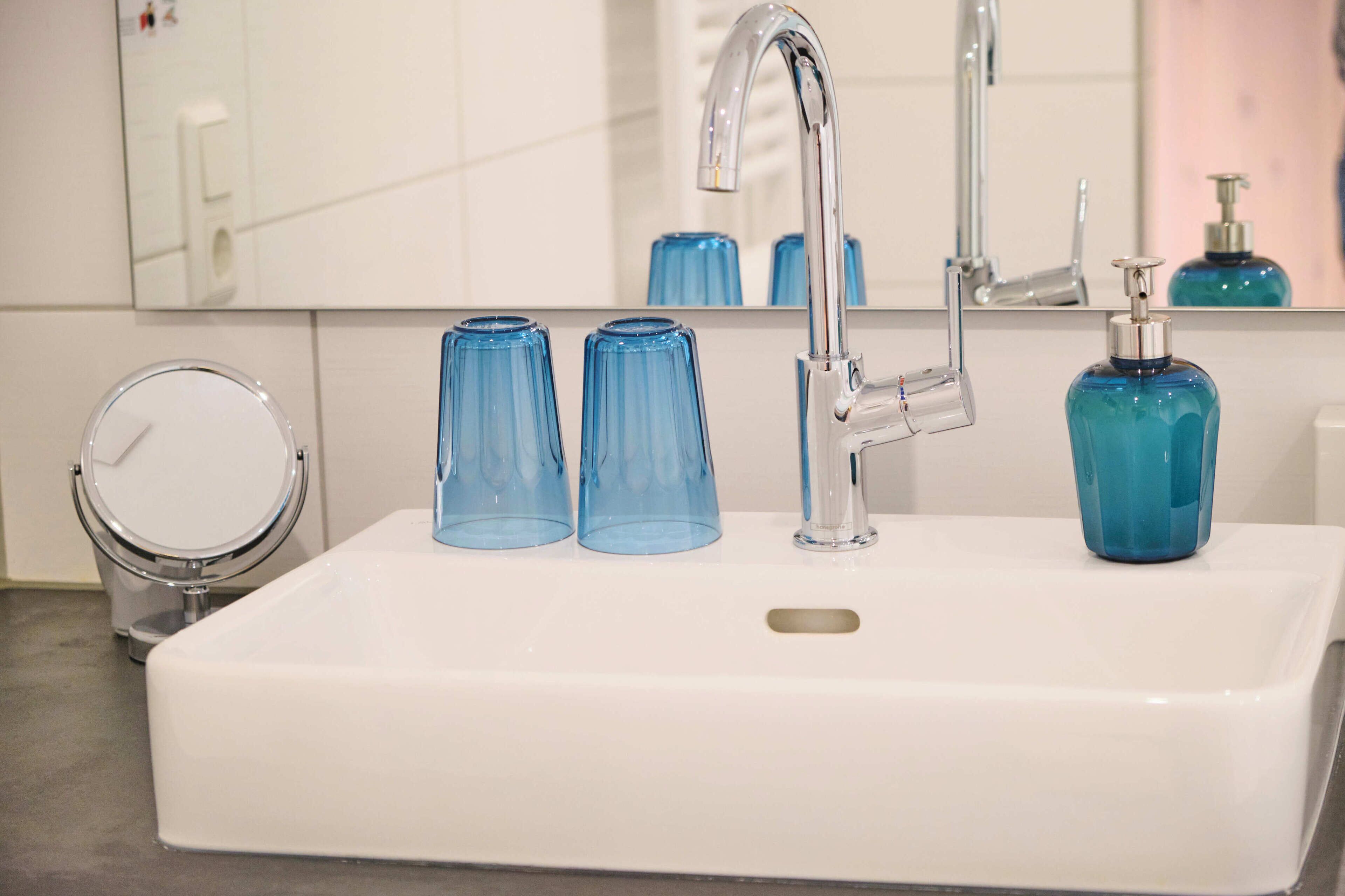 A white bathroom sink with a chrome faucet, two blue glass cups, and a blue soap dispenser.