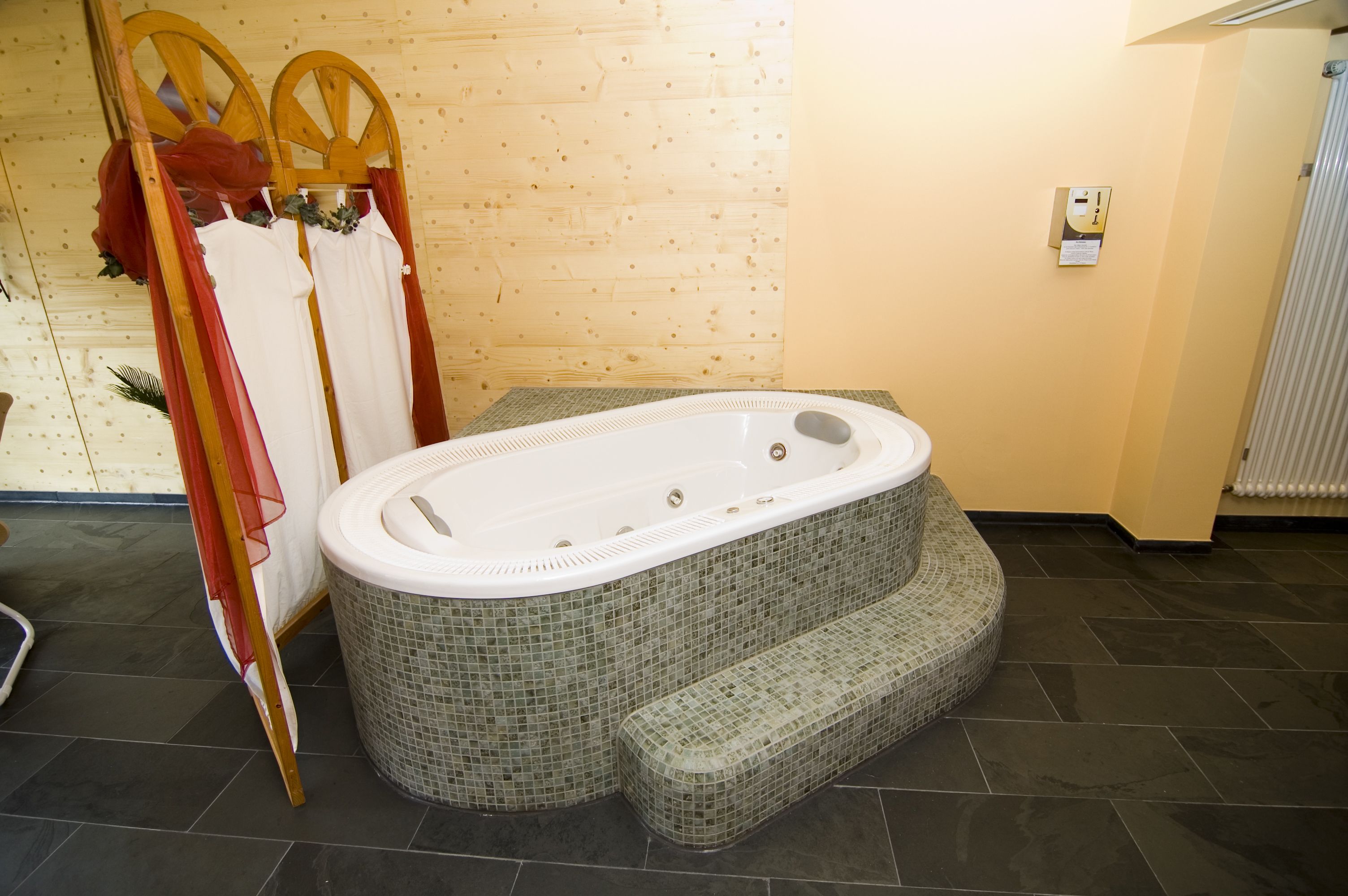 A bathroom with a large, mosaic-tiled hot tub, a wooden chair, and a shower area.