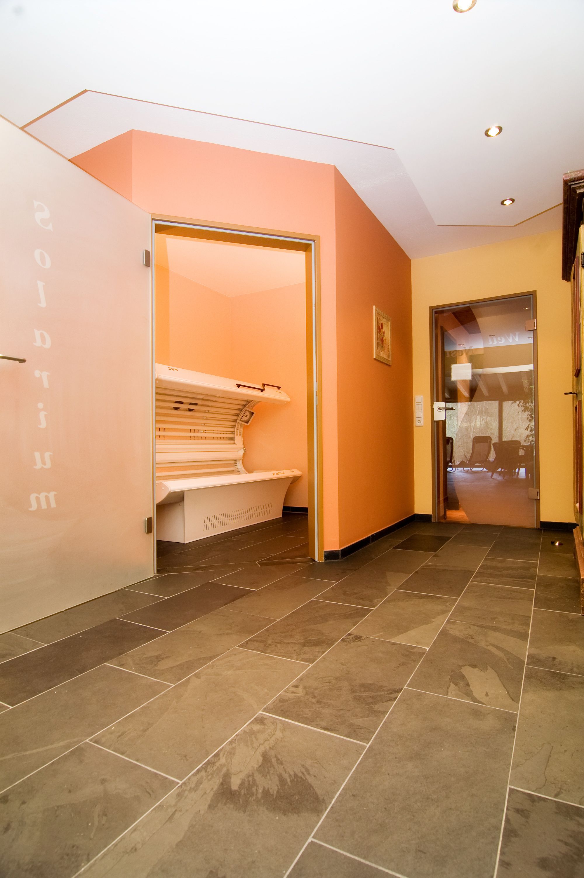 Un pasillo con una cama bronceadora, una puerta que da a una habitación y un suelo de baldosas.