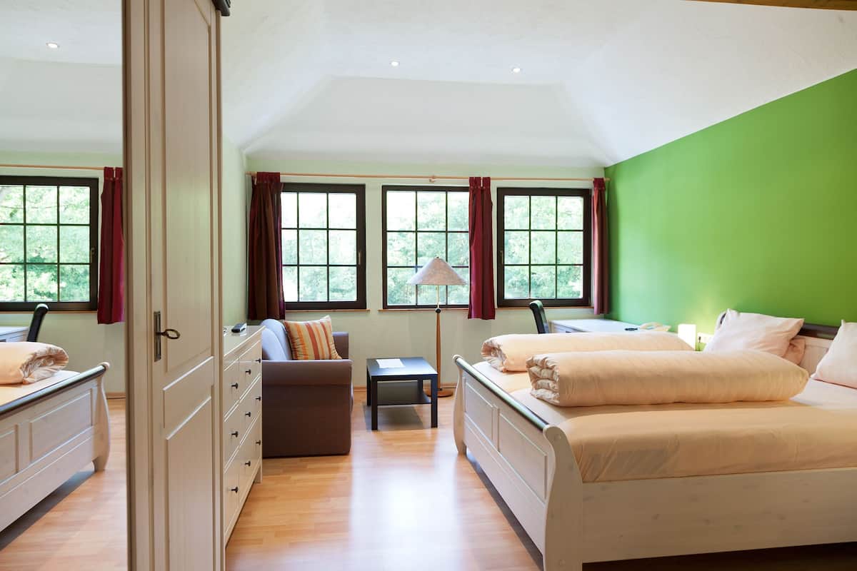 A bedroom with two beds, a sofa, a small table, and a lamp.