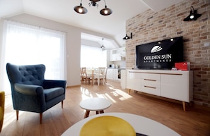 A modern living room with a large flat-screen TV, a blue armchair, a round white table, and a brick wall.
