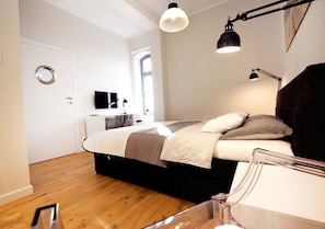 A modern bedroom with a bed, bedside lamps, a TV, and a window. - Golden Sun Apartments - Port (Kolobrzeg)