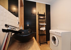 A modern bathroom with a black basin, a wooden shelf with towels, and a white washing machine.