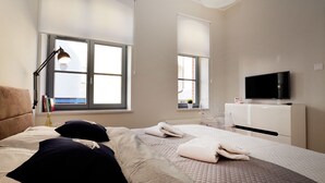 Une chambre à coucher avec un lit, des oreillers, une lampe de chevet, une télévision et une fenêtre.