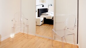 Une chambre moderne avec un plancher en bois, un lit doté d’une tête de lit sombre et deux chaises transparentes.