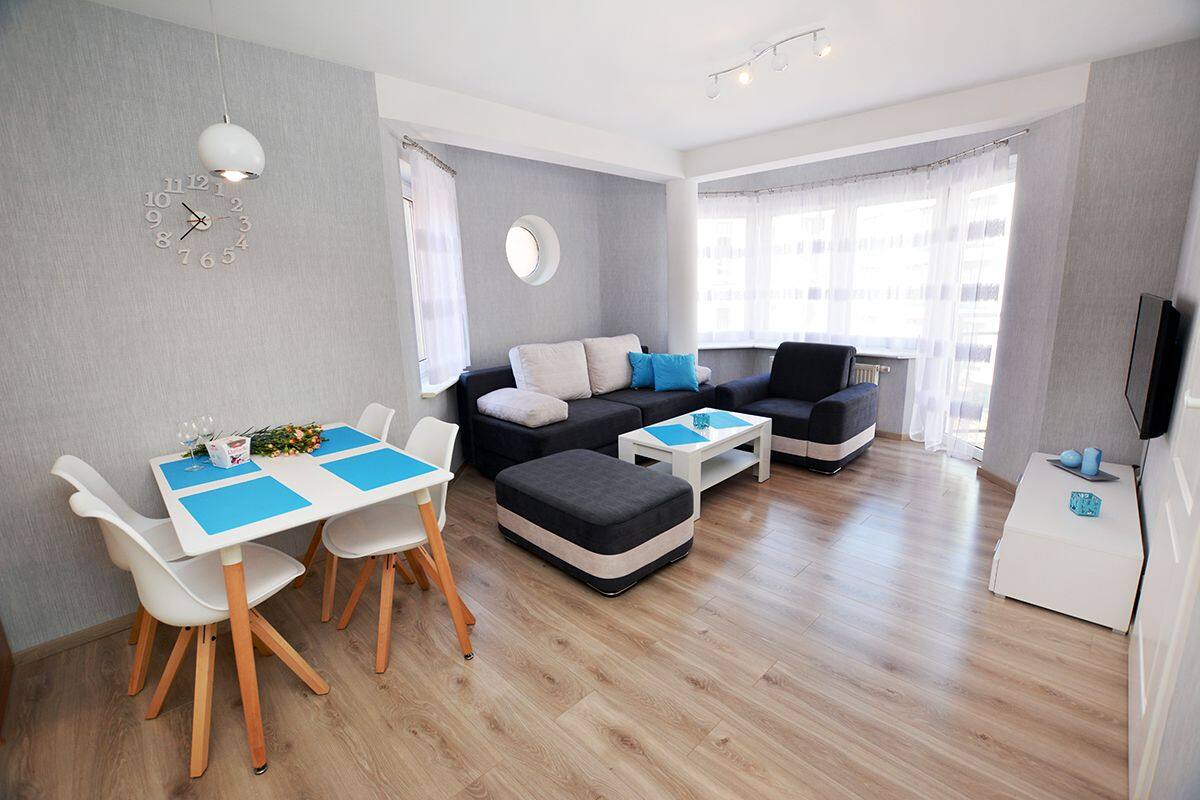 A modern living room with a dining area, grey walls, wooden flooring, and a round clock on the wall.