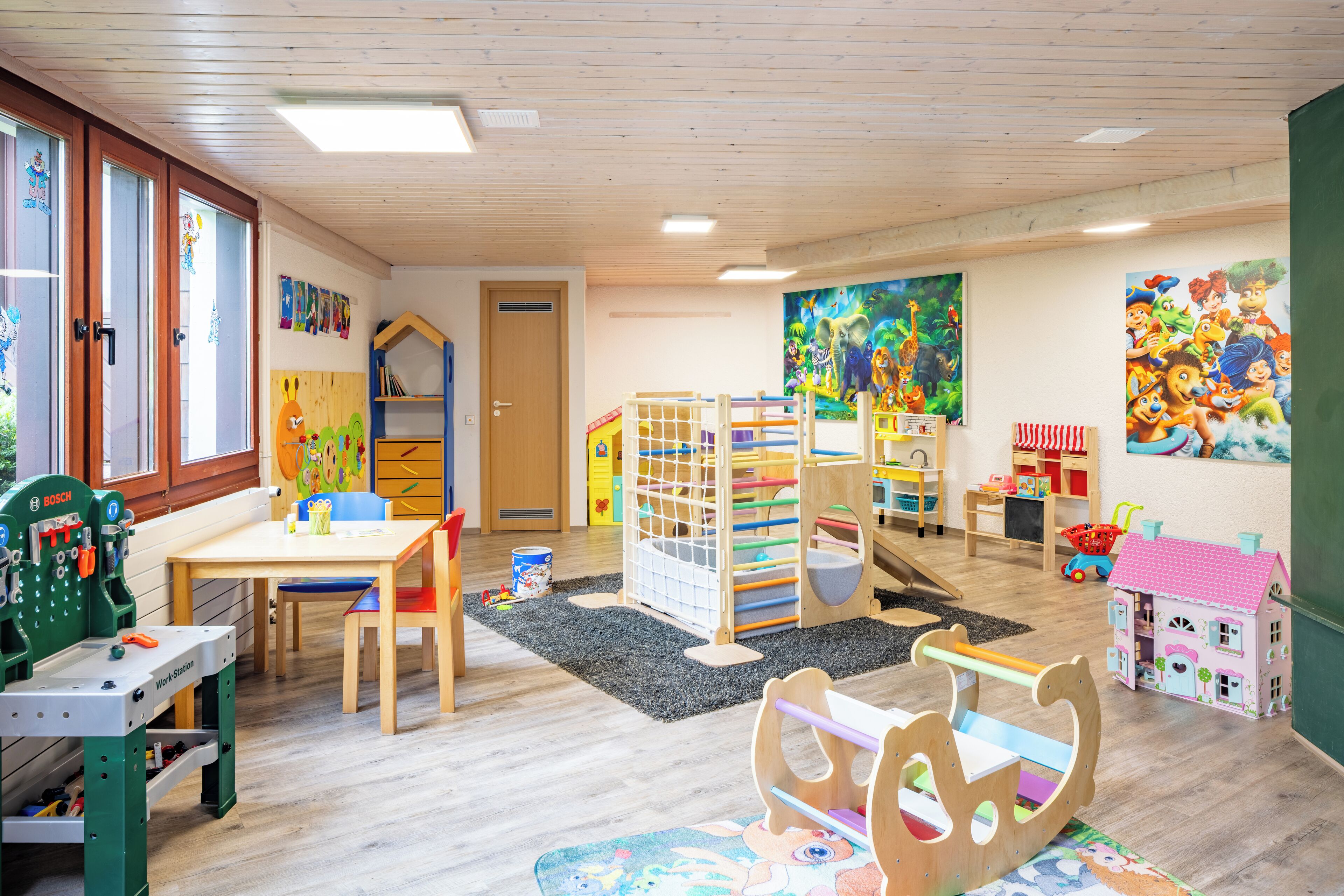 Ein Spielzimmer für Kinder mit Arbeitsbereich, Spieltischen und bunten Dekorationen.