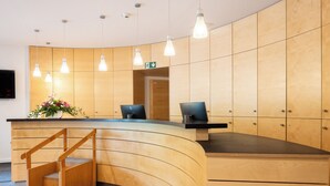 Un mostrador de recepción de diseño curvo, paneles de madera y una pequeña escalera que lleva a un nivel superior.