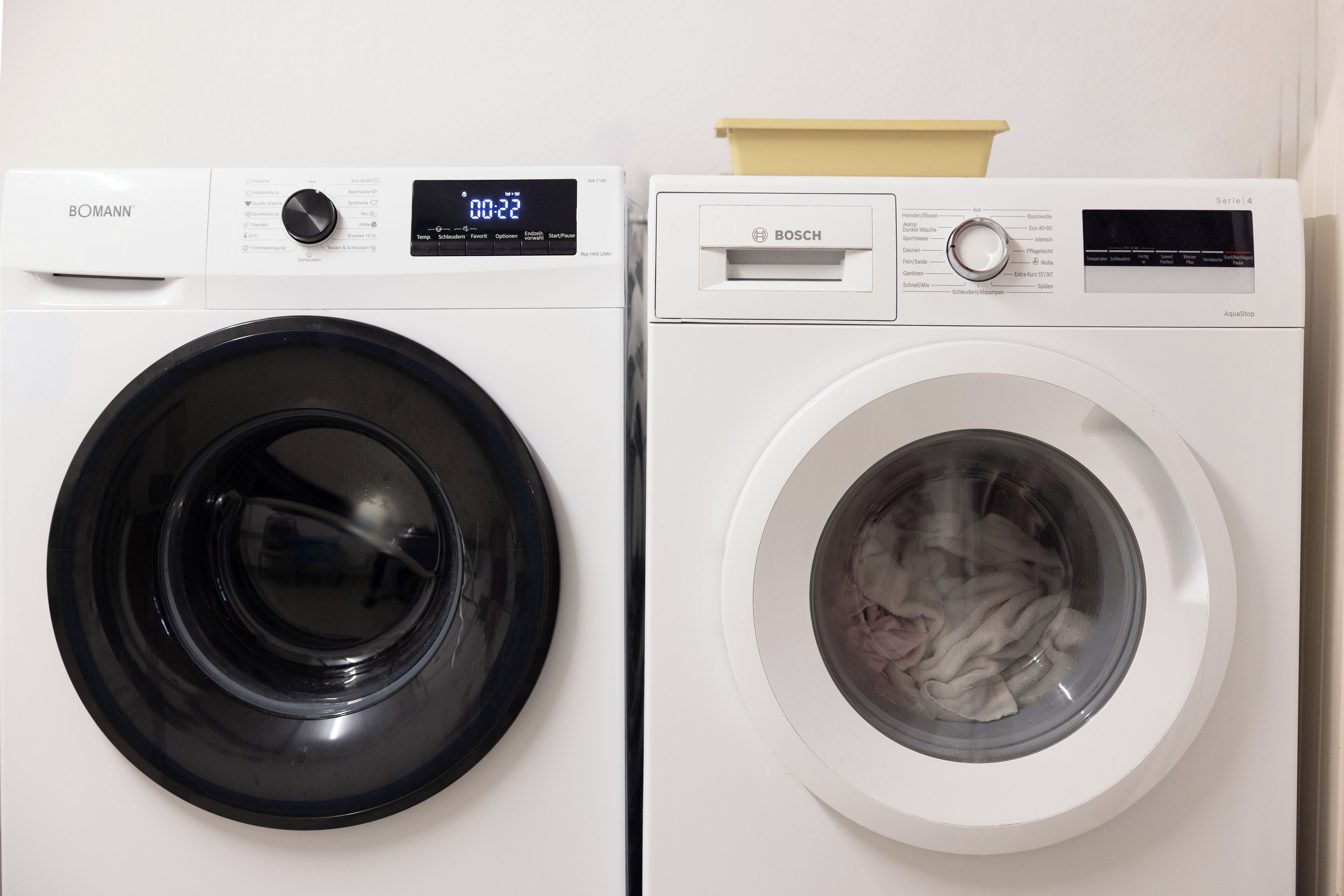 Two front-loading washing machines, one labeled 'BOMANN' and the other 'BOSCH', with a control panel and a digital display.