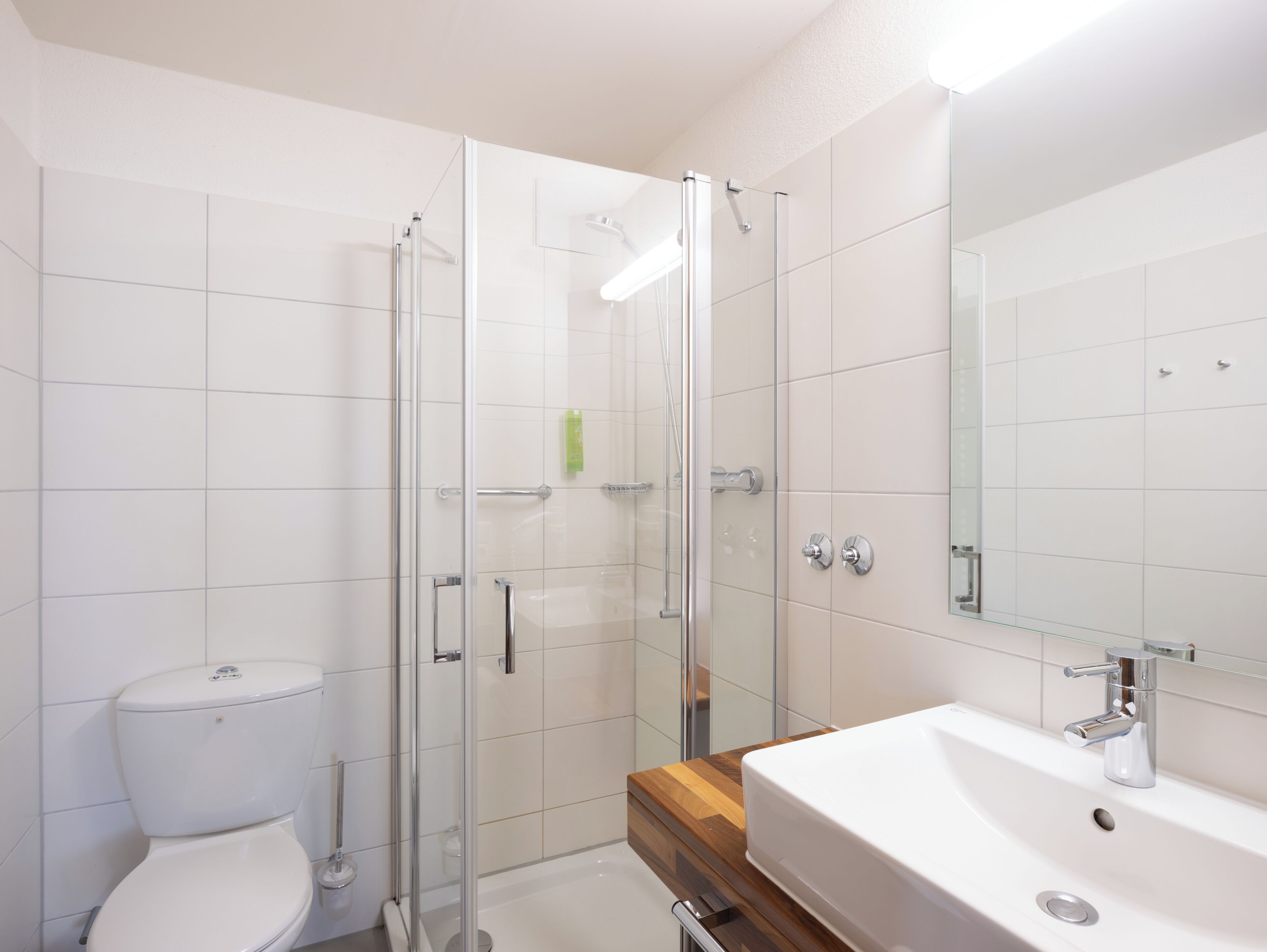 A modern bathroom with a glass shower enclosure, a white toilet, and a wooden vanity with a sink.