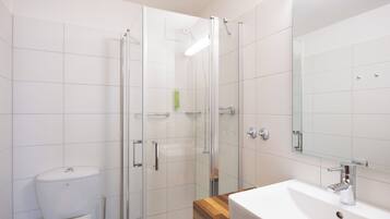 A modern bathroom with a glass shower enclosure, a white toilet, and a wooden vanity with a sink.