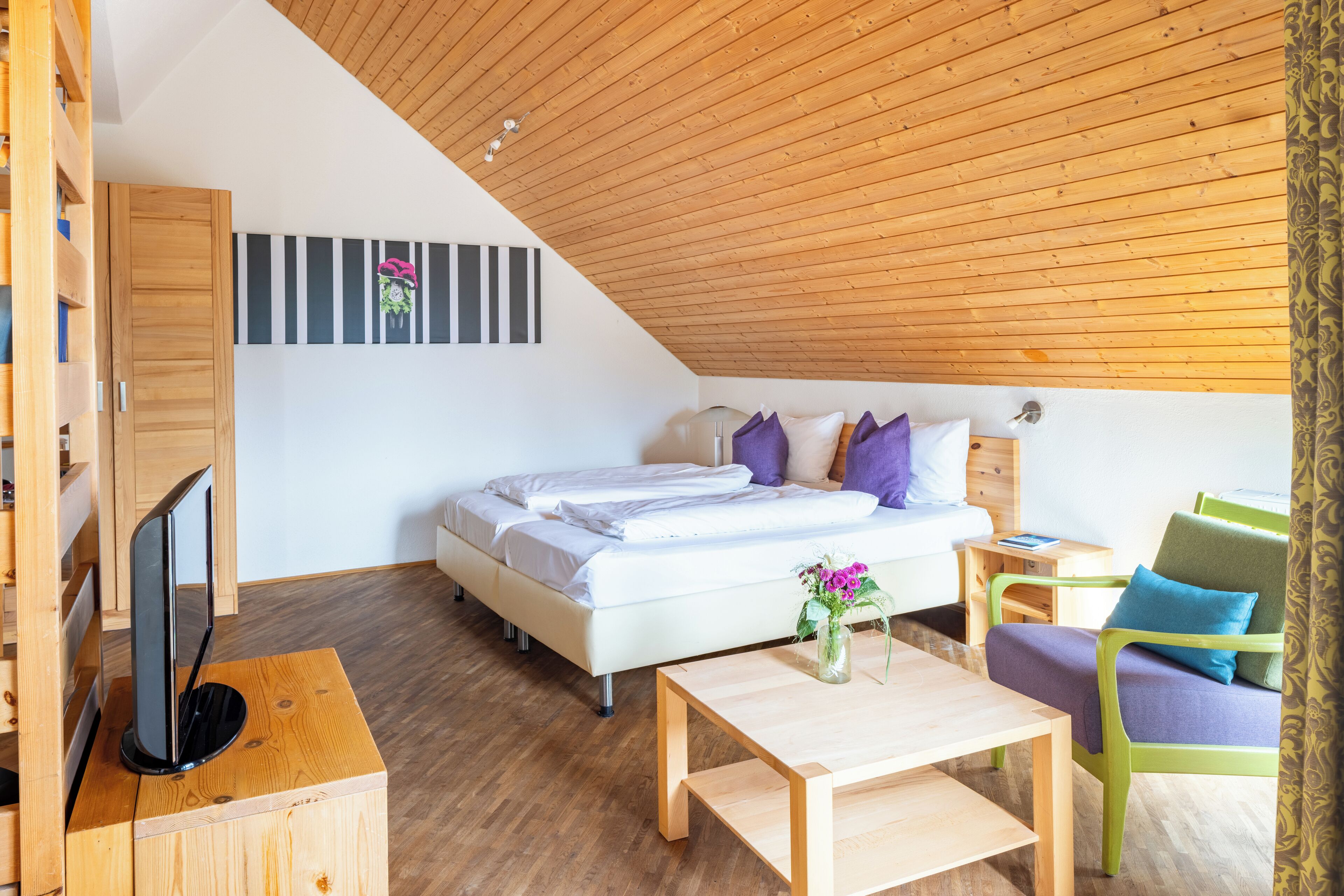 Een slaapkamer met een bed, nachtkastje, stoel en een televisie op een houten standaard.