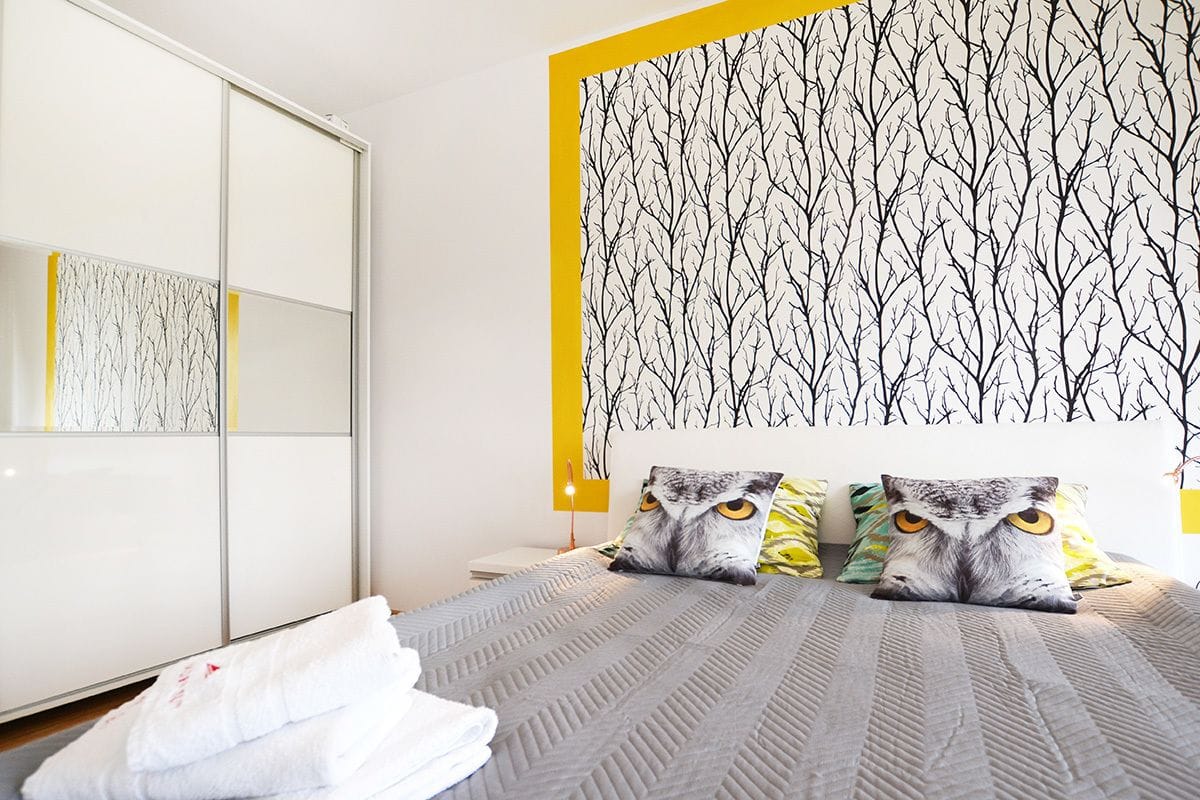A bedroom with a bed, two pillows with owl designs, a mirror, and a wardrobe.