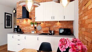 A modern kitchen with white cabinets, a brick accent wall, and two pendant lights. - Golden Sun Apartments- Polanki (Kolobrzeg)