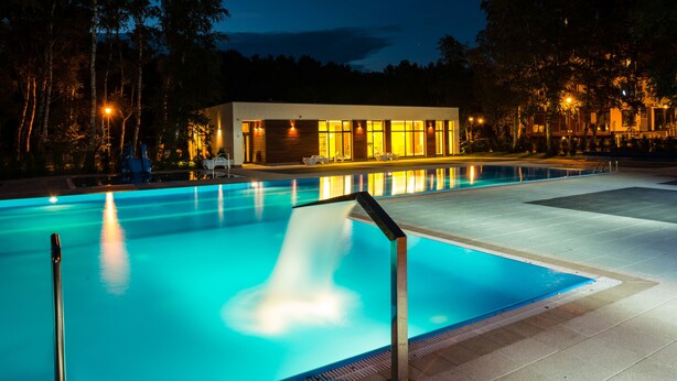 A swimming pool with a modern building in the background, surrounded by trees. - Golden Sun Apartments- Polanki (Kolobrzeg)